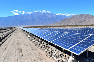 Expansive solar farm in arid landscape, snowy mountains in background