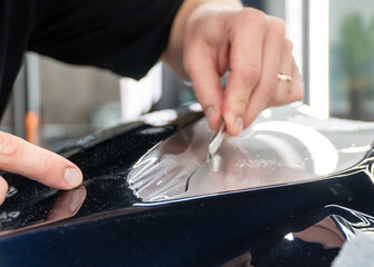 The process of installing PPF, armored film on the car. PPF is a polyurethane, protective film that protects the paint from scratches. Car wrapping, tuning, styling. Close-up, selective focus.