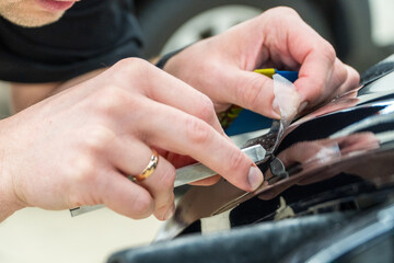 The process of installing PPF, armored film on the car. PPF is a polyurethane, protective film that protects the paint from scratches. Car wrapping, tuning, styling. Close-up, selective focus.