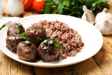 Tasty meatballs with sauce, brown rice and green onion on wooden table, closeup