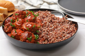 Tasty meatballs with sauce and brown rice on white tiled table, closeup