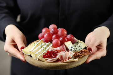 Woman holding board with different types of delicious cheese and other snacks, closeup
