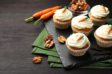 Tasty carrot muffins with cream, walnuts and fresh vegetables on black wooden table, closeup. Space for text