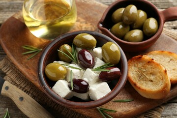 Marinated olives with feta cheese, bread pieces, oil and rosemary on wooden table, closeup