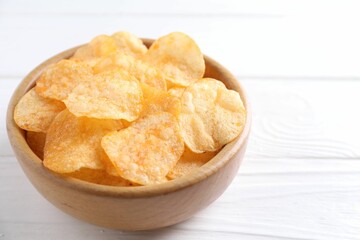Tasty potato chips in bowl on white wooden table, closeup. Space for text