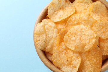 Tasty potato chips in bowl on light blue background, top view. Space for text