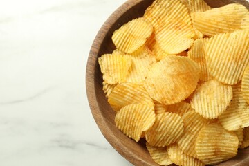 Tasty potato chips in bowl on white marble table, top view. Space for text