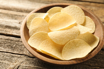 Tasty potato chips in bowl on wooden table, closeup