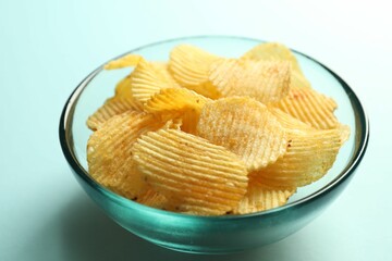 Tasty potato chips on light blue background, closeup