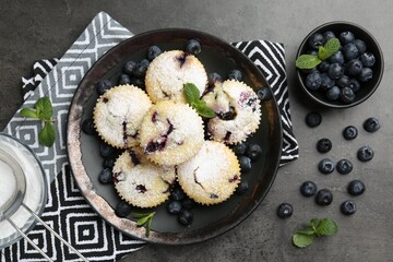 Delicious muffins with blueberries, powdered sugar and mint on dark textured table, flat lay