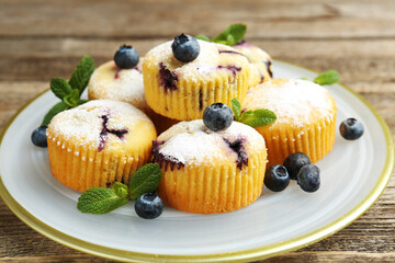 Delicious muffins with blueberries, powdered sugar and mint on wooden table, closeup