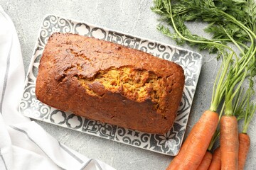 Tasty carrot cake and vegetables on grey textured table, flat lay