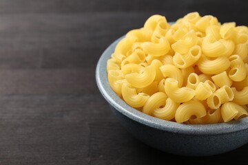 Raw horns pasta in bowl on dark wooden table, closeup. Space for text