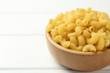Raw horns pasta in bowl on white wooden table, closeup. Space for text