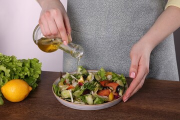 Woman pouring oil onto tasty salad at wooden table against white background, closeup