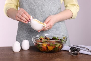 Woman pouring oil onto tasty salad at wooden table against white background, closeup