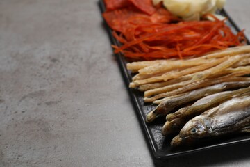 Many different dried fish snacks on grey table, closeup. Space for text