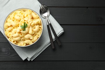 Delicious macaroni and cheese with parsley served on black wooden table, top view. Space for text