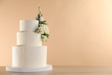 Delicious wedding cake decorated with flowers on wooden table against beige background, closeup. Space for text