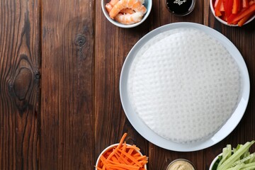 Edible rice paper sheets and ingredients on wooden table, flat lay. Space for text