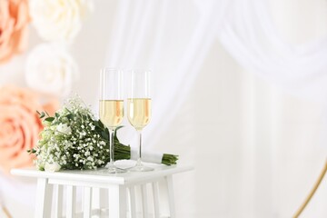 Glasses of champagne and wedding bouquet on table indoors, space for text