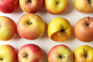 Rotten apple among fresh ones on white wooden table, flat lay