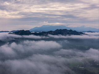 An wide Aerial view of a mountainous landscape with green fields and a village in the foreground. The mountain dominates the background, partially covered by clouds. Tana Toraja - Indonesia 