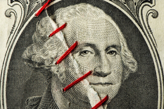 Close up of torn ripped United States Dollar bill torn and sewn stitched back together with red thread