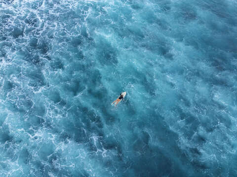 Aerial 90 degree straight down drone photo of a young female surfer on a surfboard in the emerald ocean water. Pacific Coast, El Tunco, El Salvador, Central America.