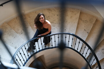 Attractive middle aged caucasian woman wearing a black jump suit in an elegant setting. She is walking down a spiral staircase made of marble. Luxury lifestyle, 