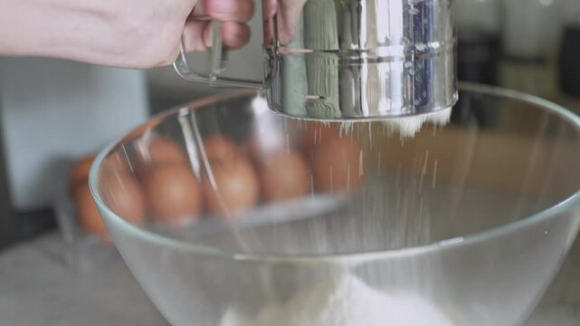 Hand sifting flour into glass bowl with metal sifter