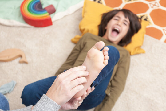 Playful child laughing while his mother tickles his feet &ndash; overhead view