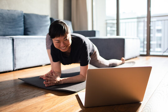 Woman sitting on yoga mat in the living room having video call on laptop