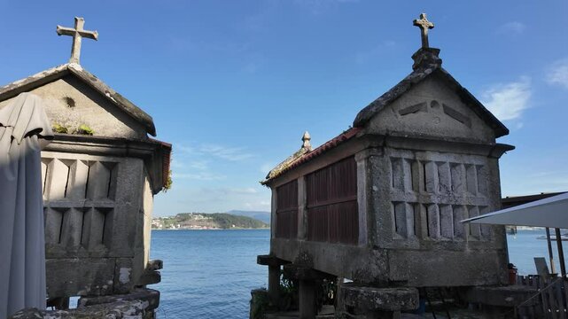 Traditional galician granaries, known as horreos, stand on stilts by the water's edge, topped with stone crosses in combarro, spain