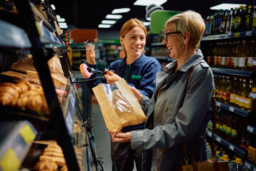 Happy supermarket worker assisting senior woman in choosing pastry at store.