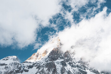 A snow covered mountain peak near Zermatt, Switzerland, partially obscured by clouds. Jagged...