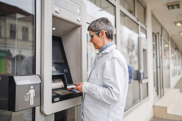 mature woman use credit card and withdrawing cash at the ATM outdoor