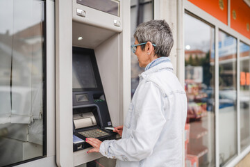 mature woman use credit card and withdrawing cash at the ATM outdoor