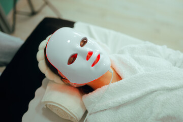 Woman Getting Red Light Therapy for her Skin with Mask. Lady using professional services in a beauty salon for skin care 