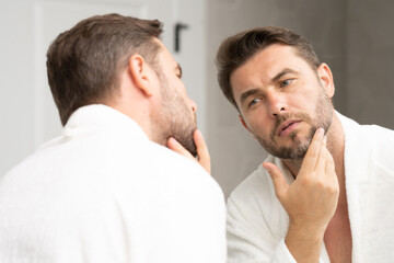 a well-groomed adult man looks in the mirror for well-groomed, wrinkle-free skin. Handsome man...