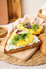 Wooden board with tasty scrambled eggs sandwich on light background