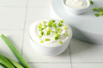 Bowl with sour cream and sliced green onion on white tile table