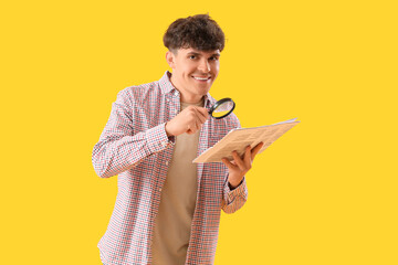 Young man with magnifier and newspaper on yellow background