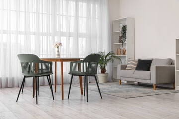 Interior of modern living room with table, chairs, sofa, houseplants and shelving unit