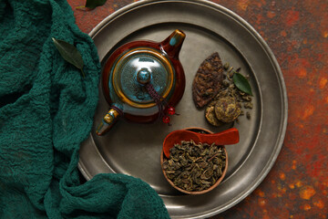 Steel tray with ceramic teapot and bowl of aromatic puer tea on brown background