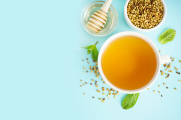 Cup of tasty buckwheat tea, honey and mint on blue background
