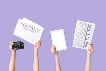 Female hands with newspapers, photo camera and tablet computer on lilac background