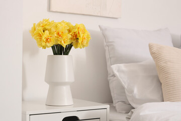 Vase with beautiful yellow narcissus flowers on bedside table, closeup