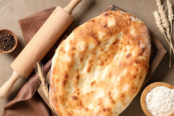 Wooden tray with tasty lavash, rolling pin, peppercorns and flour on brown grunge background