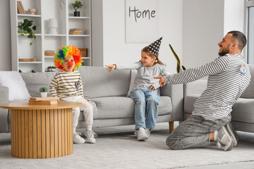 Happy father and daughter laughing at boy in clown wig at home. April fool's day prank